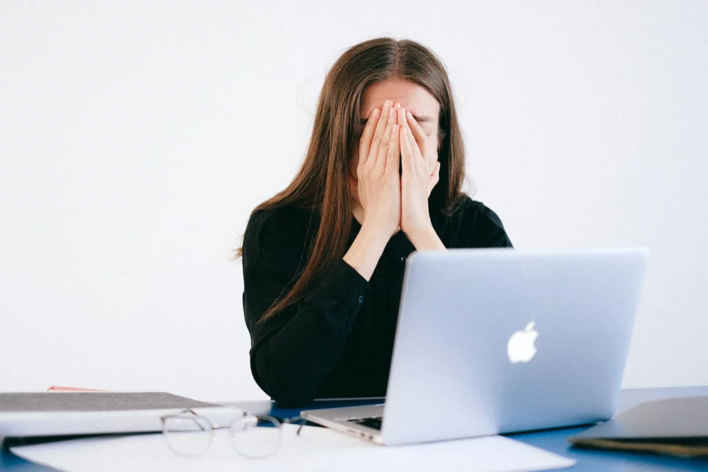 Woman With Hands on her Face in front of a Laptop